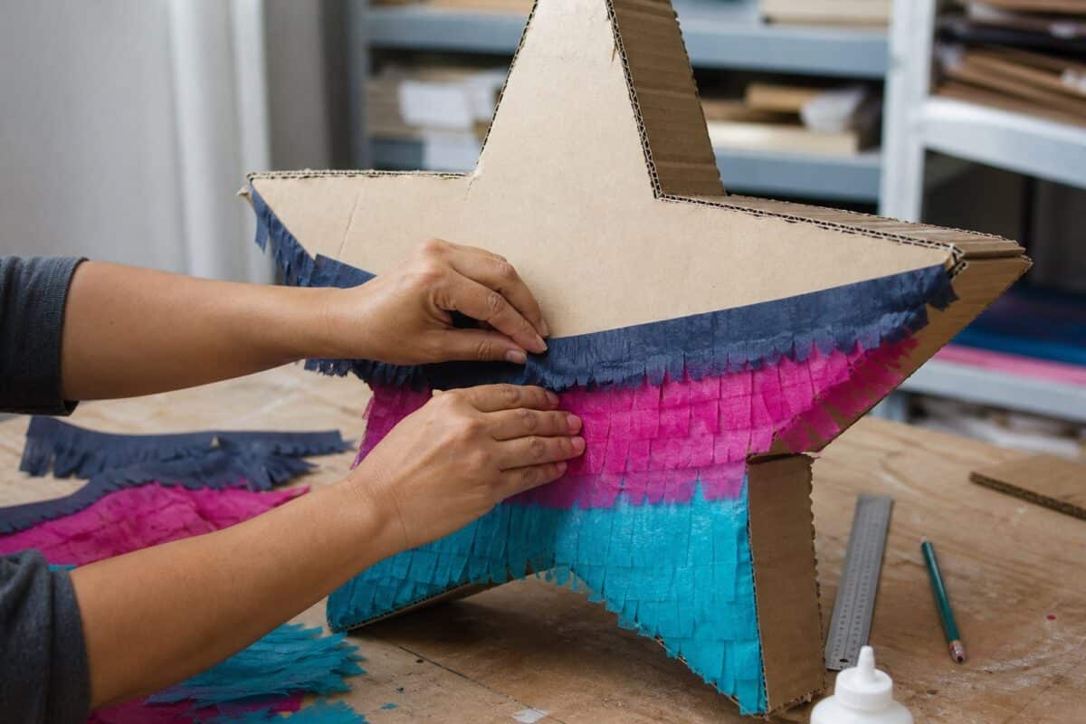 Illustrative close-up of hands applying tissue paper fringe to a cardboard star pinata